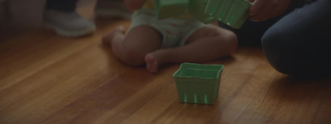 A parent sitting on the floor giving their child baskets to play