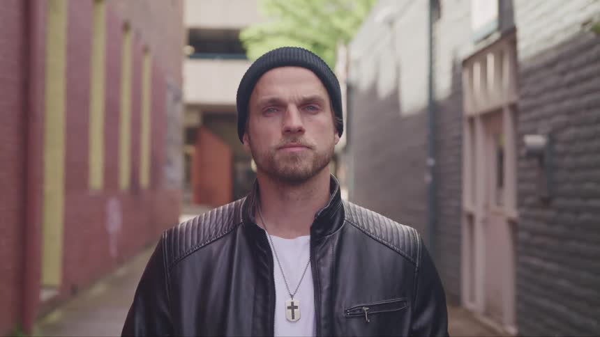 A man with a jacket and a hat in an alleyway standing and staring