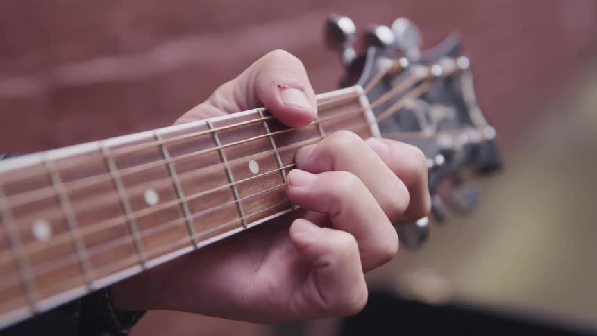 Musician is moving fingers over the guitar strings and frets