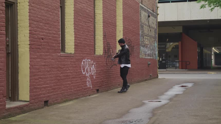 A man is smashing his guitar against a wall of a building