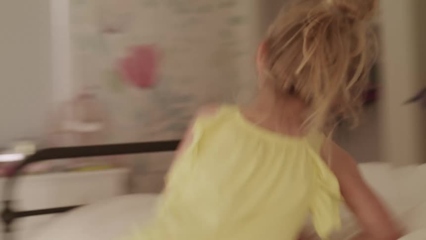 Young blonde girl walking through the rooms of a house jumps over a bed