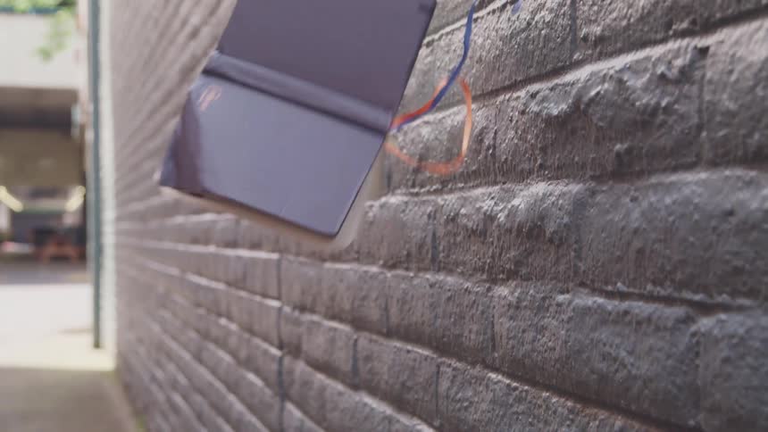 A purple book is thrown from off camera at a wall on a street