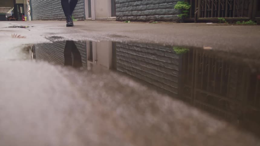 A person walking by a puddle on concrete in an alley
