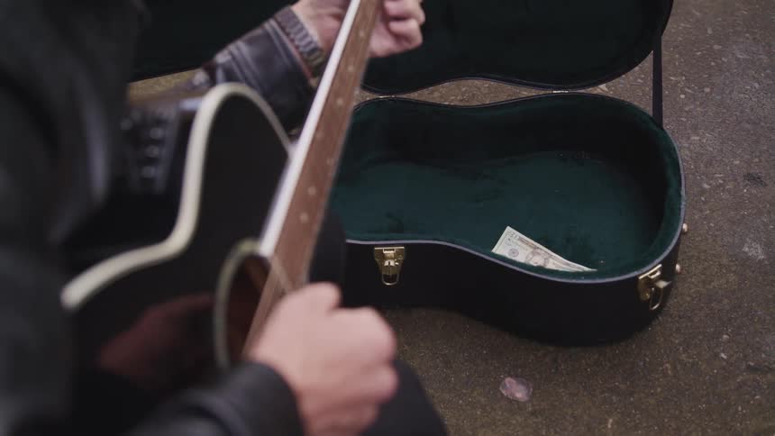 A man plays a guitar on a street and a woman puts some money in his guitar case