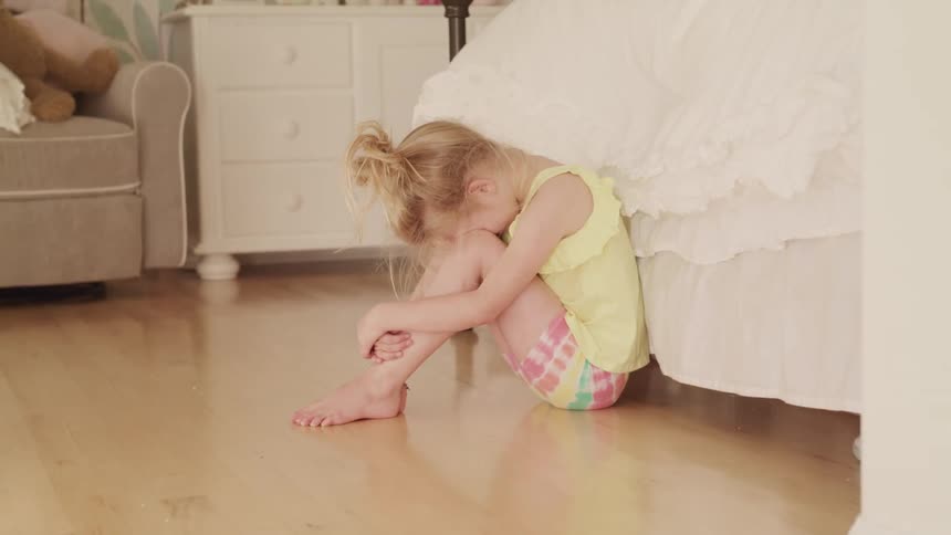 A young girl crying while sitting on the floor of a bedroom