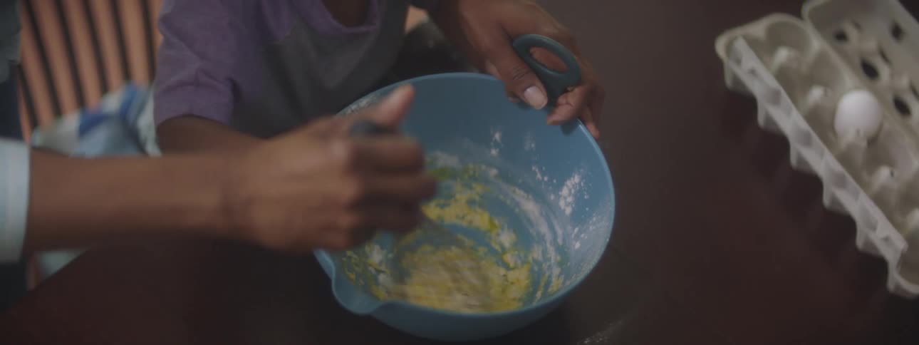 A woman helps her child stir batter as they bake at home