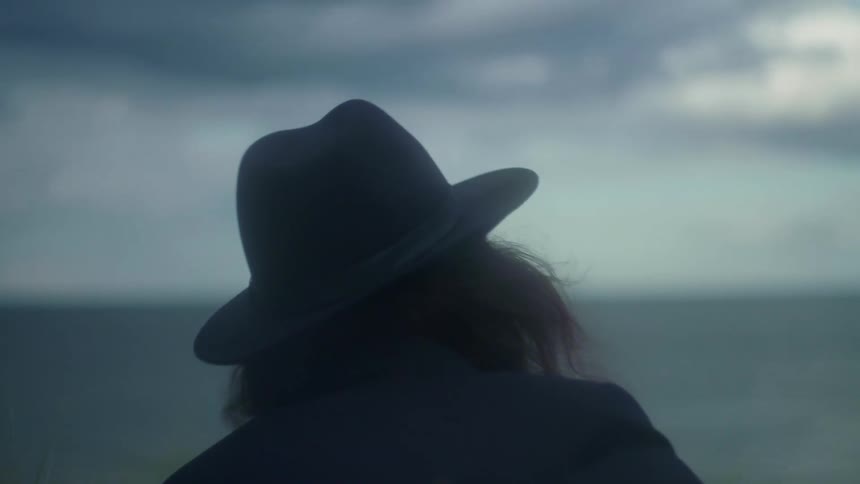 A person in a hat plays guitar near the shore on a windy day