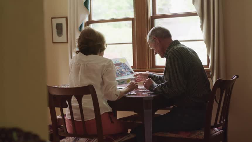 Older couple sitting at table near a window working on a puzzle