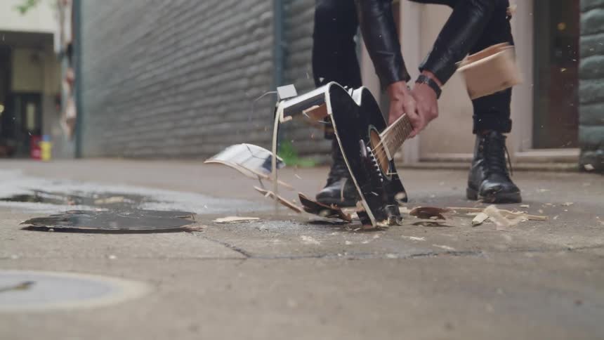 Musician smashing acoustic guitar on concrete sidewalk