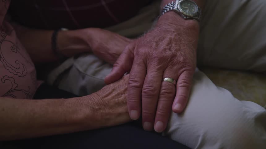 A man and a woman in a room sitting on a couch holding hands