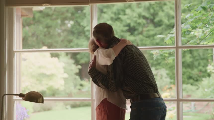 An elderly man and woman lean in for a strong hug