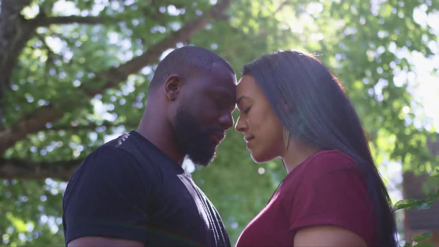 A couple standing with their foreheads touching outside on a sunny day