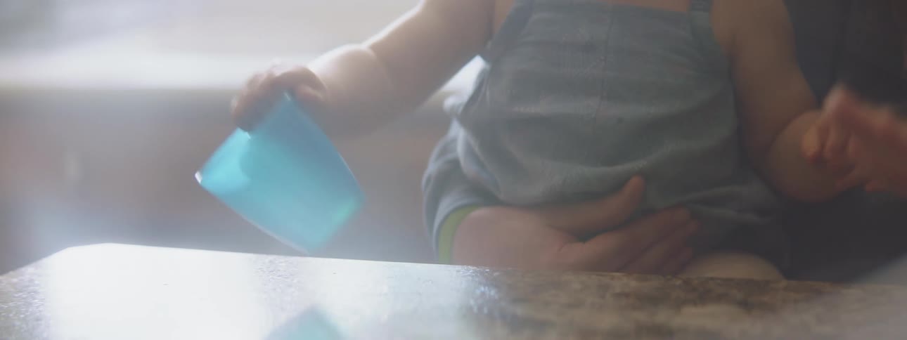 A baby banging a blue plastic cup on a table