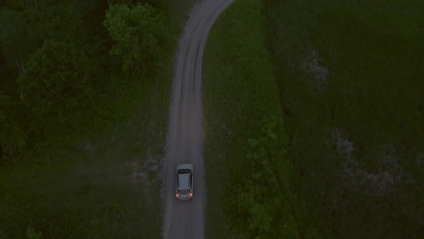A vehicle driving down a road next to a grassland