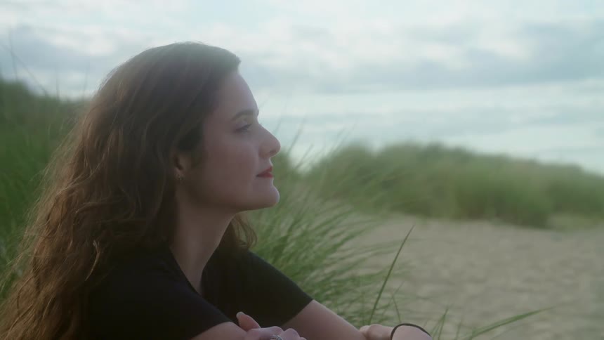 A young proud woman sits on a beach and smiles