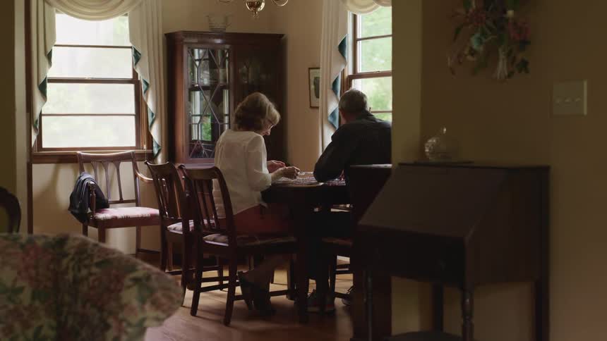 A man and a woman sitting on chairs at a table with walls and windows in the background