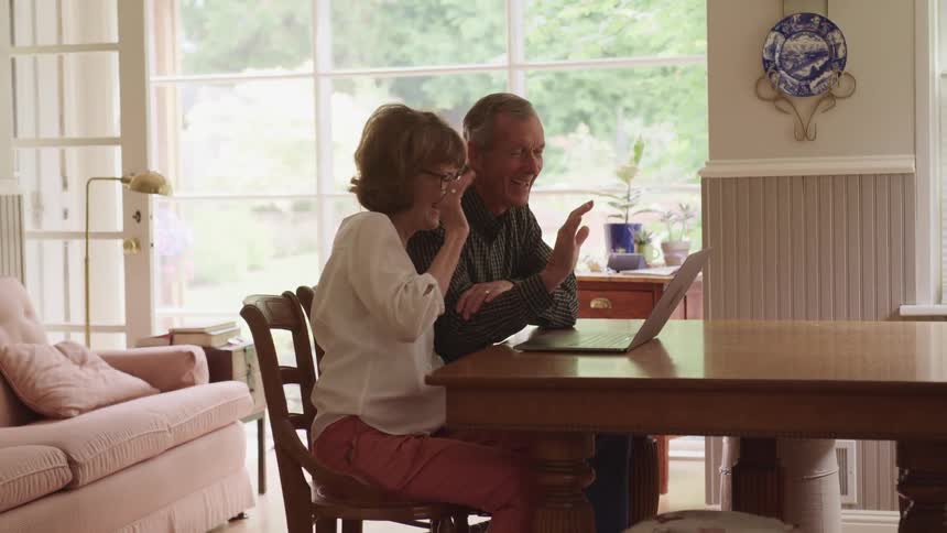 A man and a woman sitting on chairs at a table video chatting on a laptop