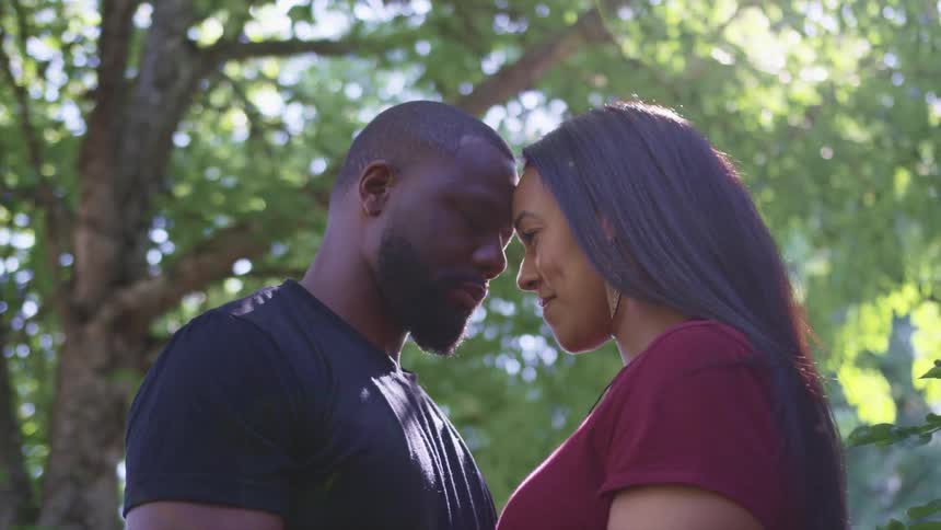 A man and a woman standing with their foreheads touching with trees the sky and clouds in the background