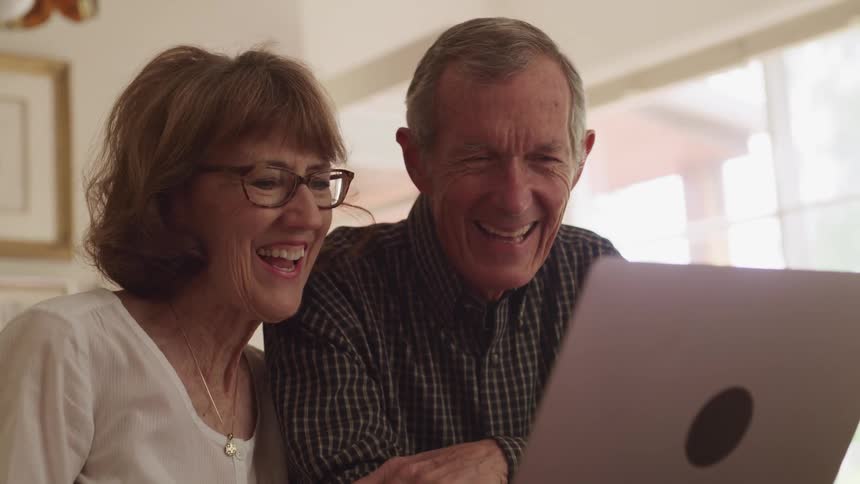 A man and a woman in a room sitting at a table video chatting on a laptop