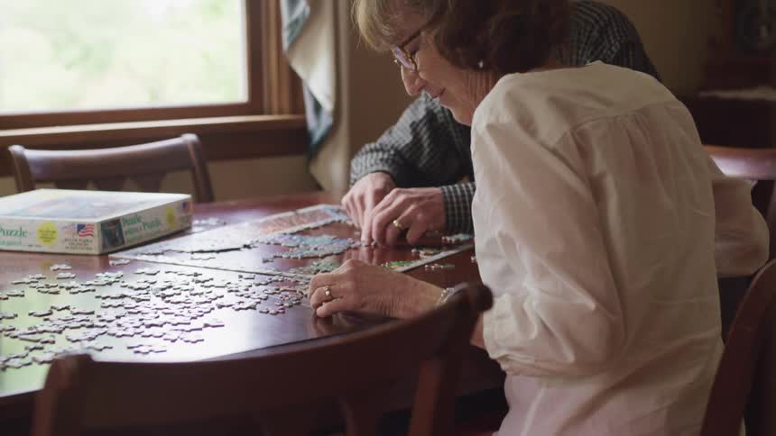 Elderly couple put togheter a jigsaw puzzle over the bed in a room at home
