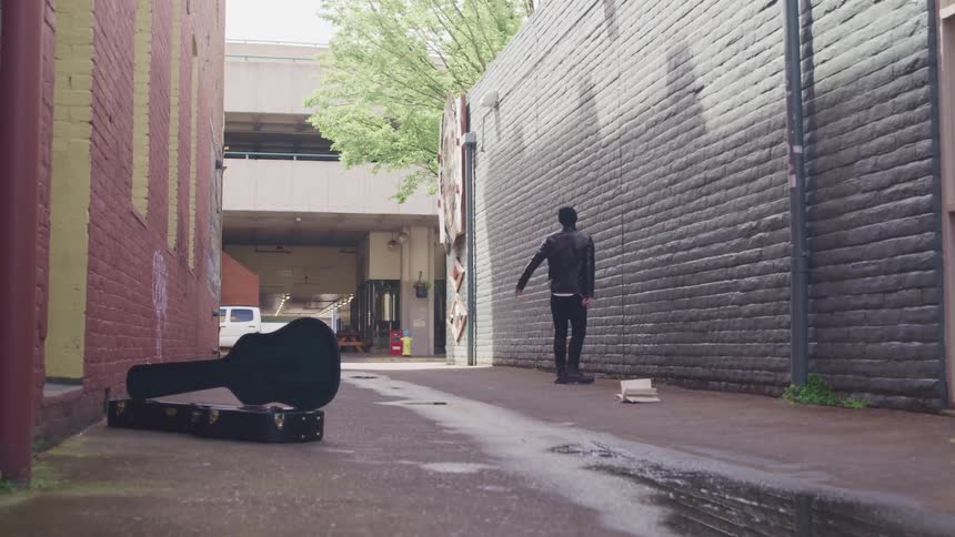 Depressed and sad man reclines against a brick wall in an alley between buildings
