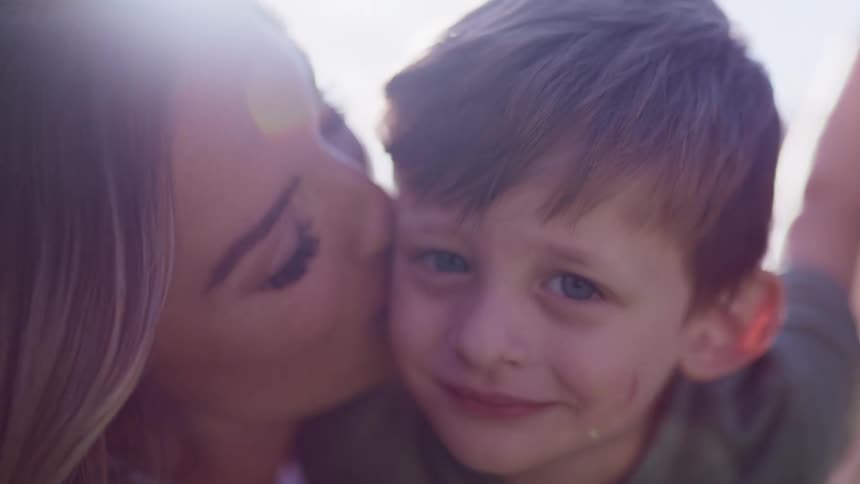 A mother kissing her son on the cheek outdoors