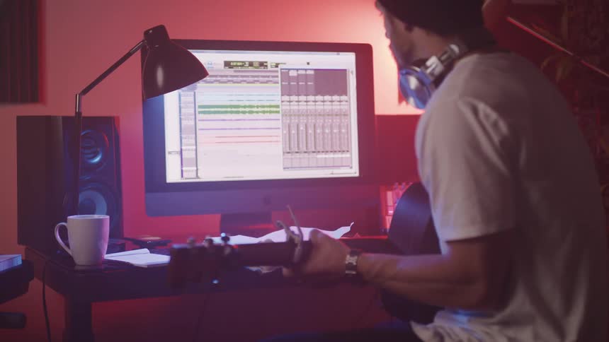 A man is playing guitar in front of his computer monitor