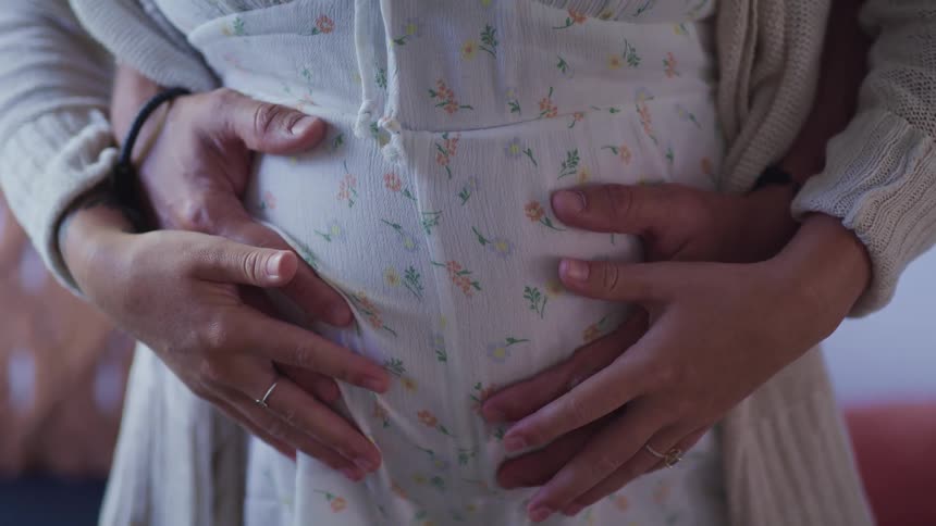 A man in a room hugging and holding a woman while rubbing her pregnant belly