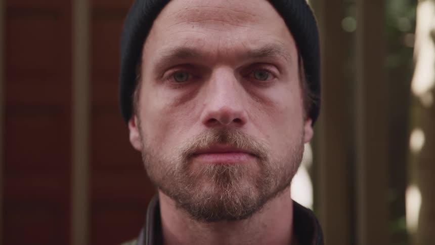 Young bearded man wearing a black beanie turns around to look at the camera