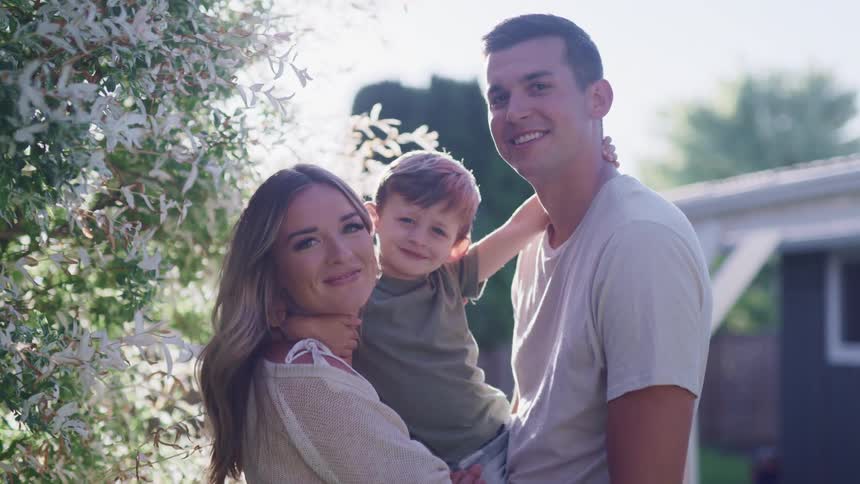 A man and woman stand outside their home and hold their young son in their arms