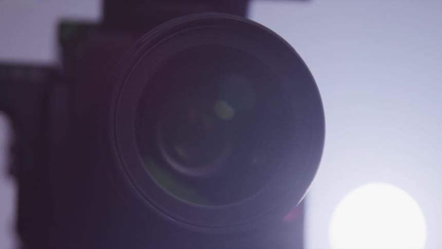 Close up of the silhouette of a turning video camera lens inside a room