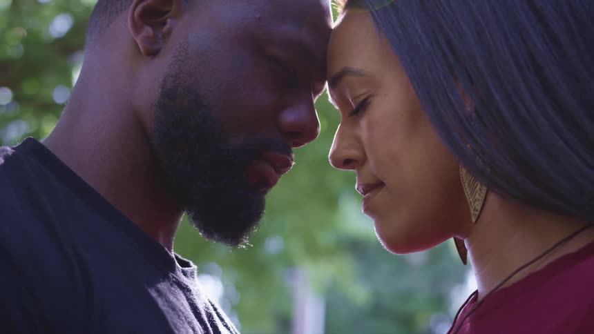 Profile of a black couple standing touching foreheads outdoors