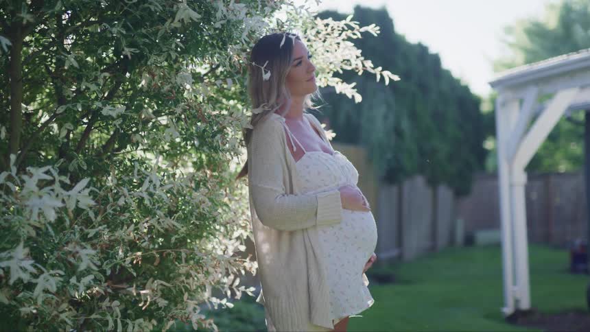A pregnant woman is standing outdoors in spring
