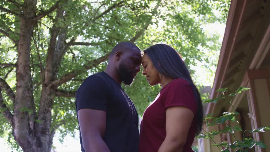 A couple standing outside with their foreheads touching on a sunny day