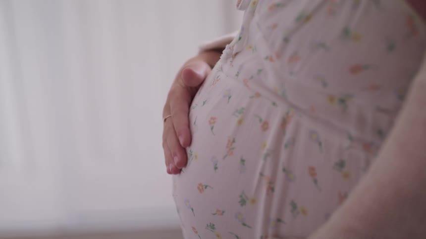 A pregnant woman in a room rubbing her belly