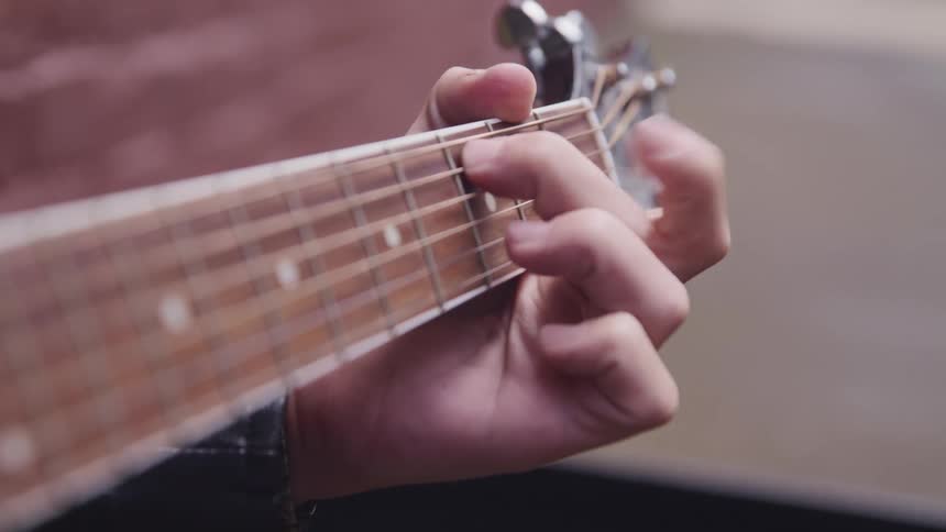 Musician is moving fingers over the guitar strings and frets