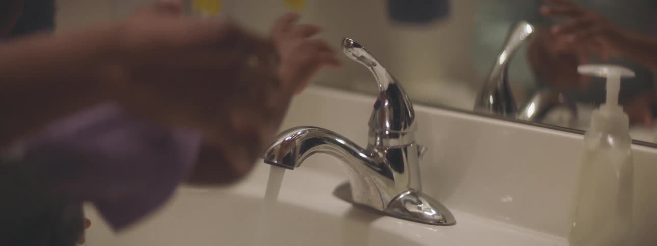 A woman helps her son wash his hands in their bathroom sink