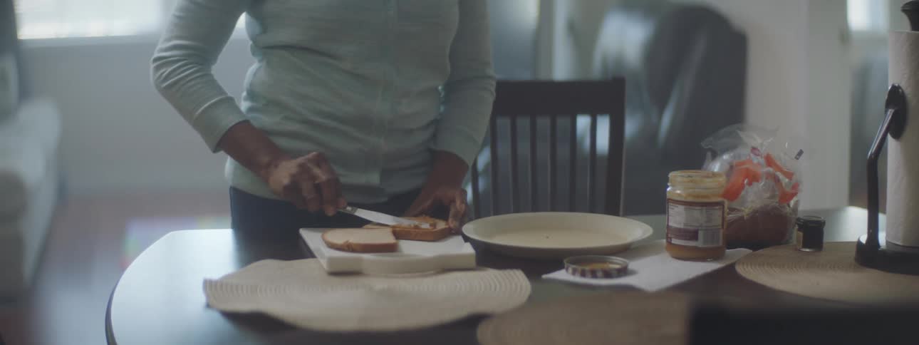 Young woman making a peanut butter jelly sandwich over the kitchen table at home