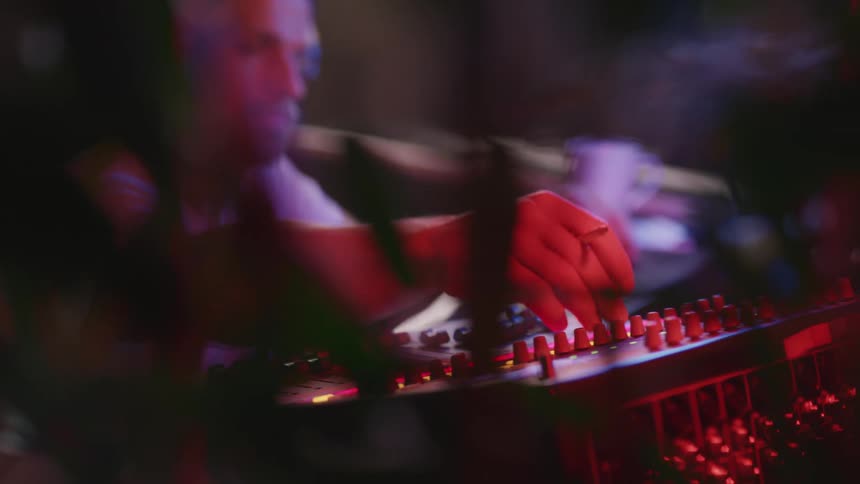 A man with a hat and headphones and a cigarette in his hand turning dials on a mixer