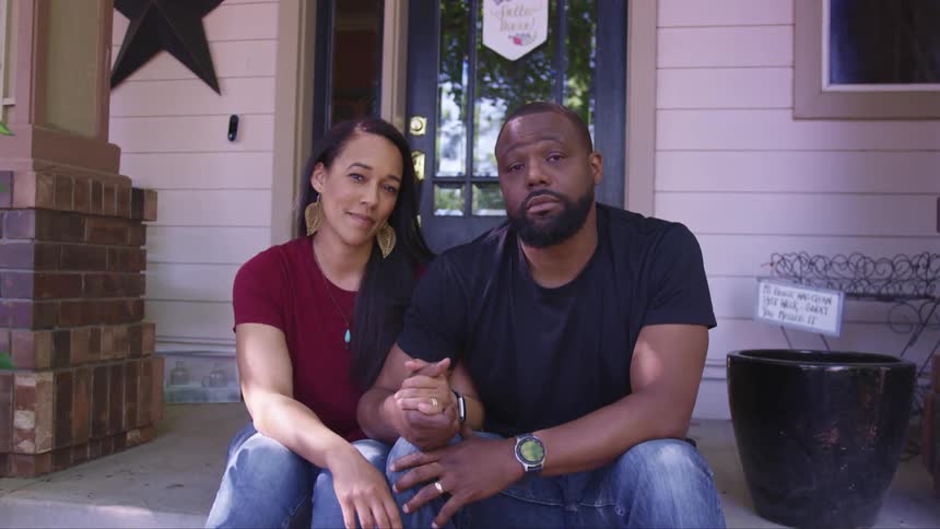 A man and a woman sitting on a porch in front of a house holding hands