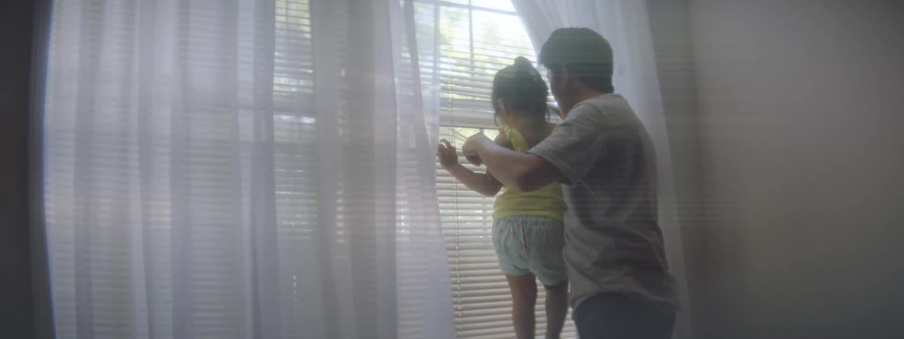 Father and daughter looking out the window through the blinds in a room at home