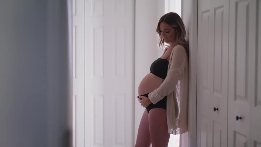 Pregnant woman leaning on wall rubbing her belly