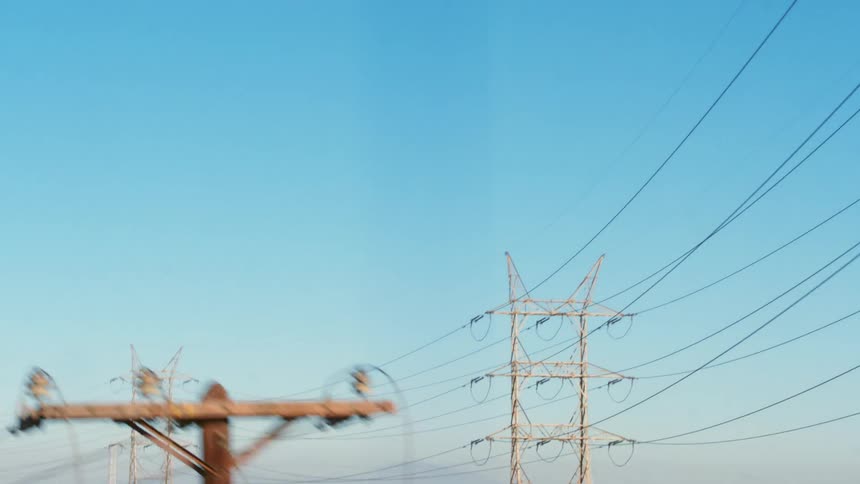 A row of utility towers loom over the small buildings near a flood control channel