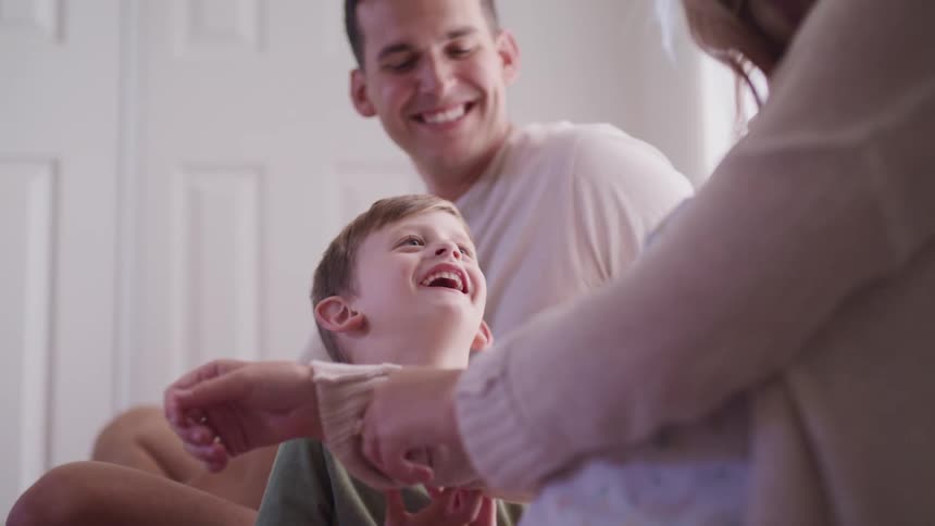 A mother and father sit with their son who is playing with the sleeve of the mothers sweater