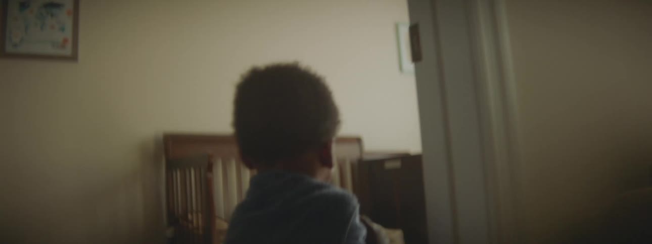 Young boy wearing a blanket as a cape runs around the rooms of a house jumping