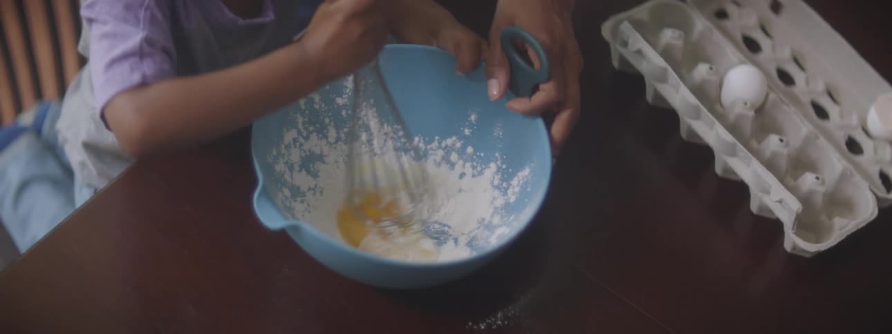 A person and a child at a table mixing eggs and flour in a bowl