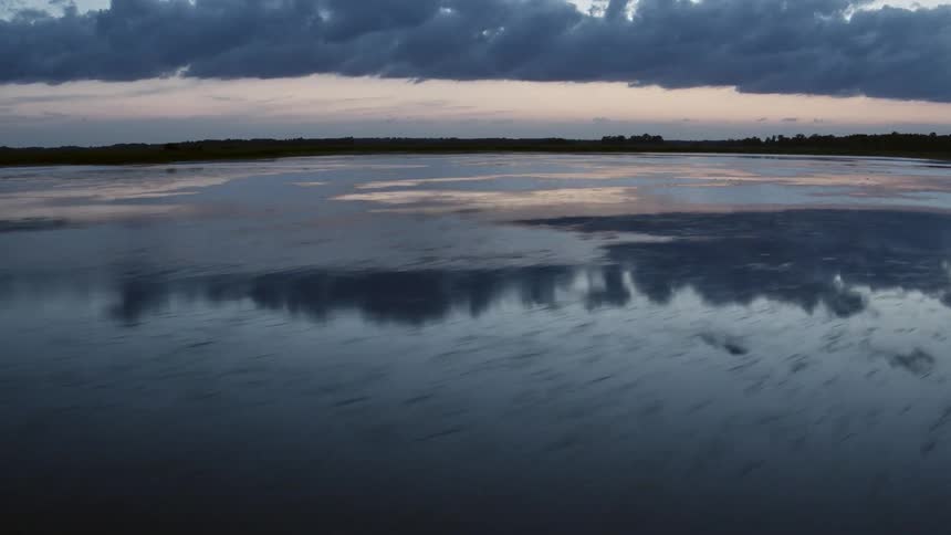 Aerial view of the calm waters of a lake near a forest at sunset