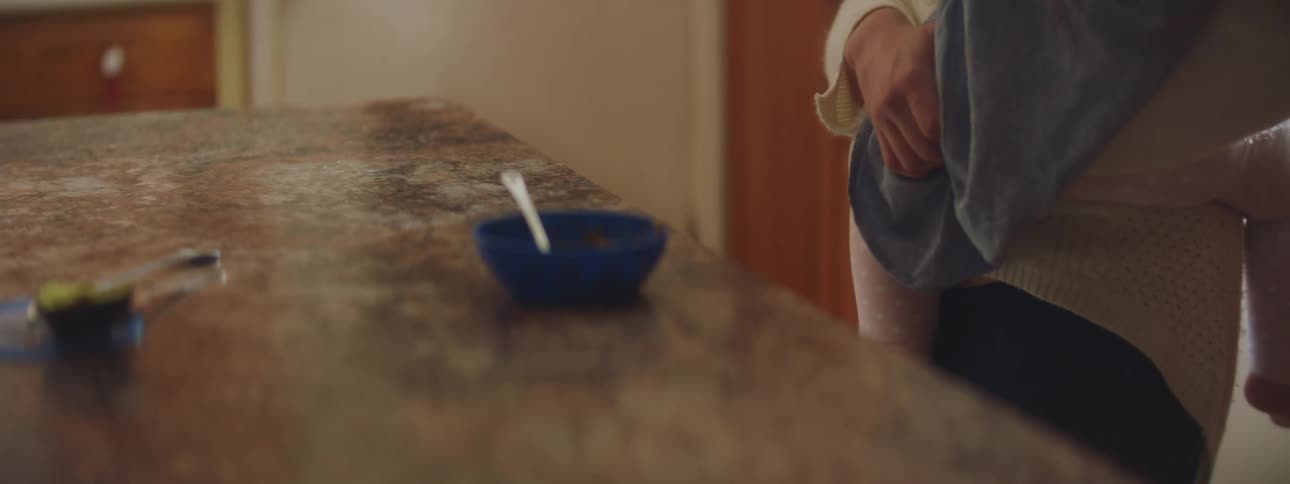 A woman in a room holding a baby next to a counter with a bowl and a spoon