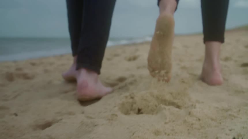 Close up of a man and womans feet as they walk along the beach