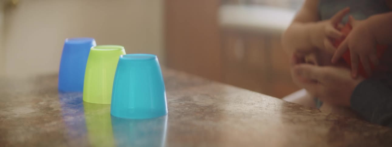 A young baby reaches out to grab at some plastic cups while it is being held by an adult